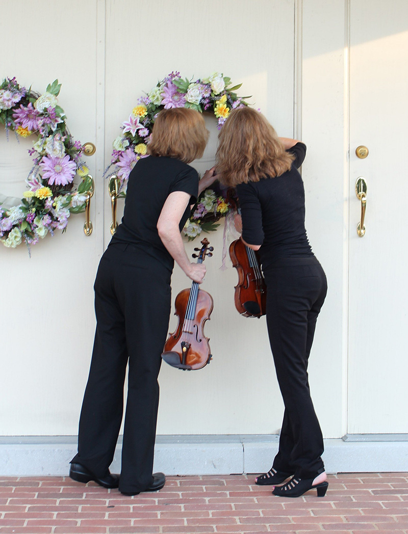 Members of Jolie Deux RVA Violin Duo looking at wreaths on church door